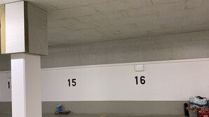 A parking garage with numbered parking spaces, concrete pillars, and a fluorescent light fixture.