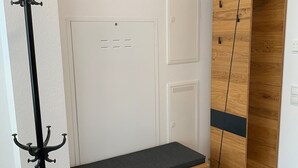A room with a wooden bench, a coat rack, a wardrobe, and a door with a vent.