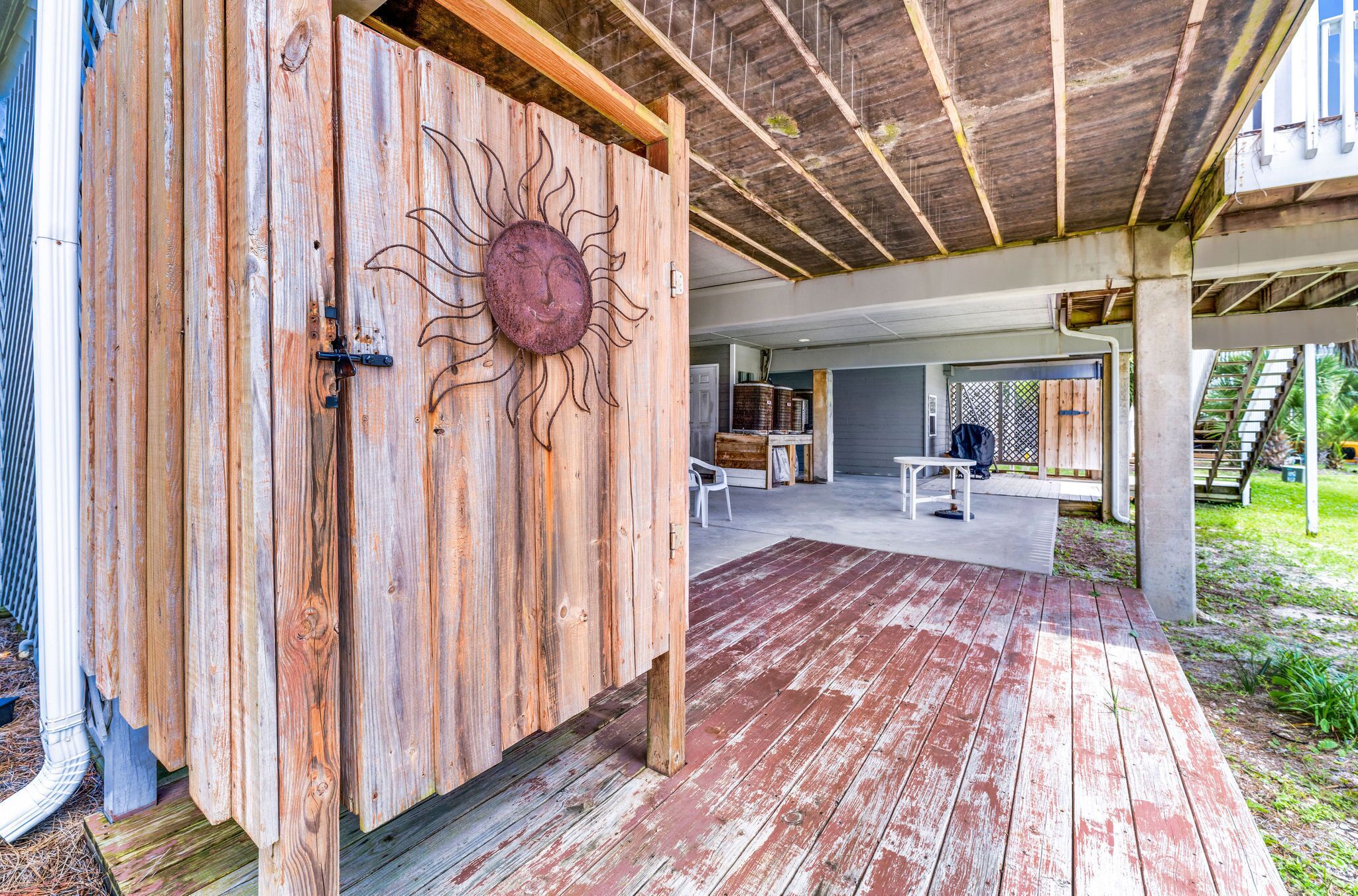 A wooden door with a sun design, a covered patio with a concrete floor, and a staircase leading to a second level.
