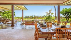 A covered outdoor dining area with a view of a landscaped garden and mountains.