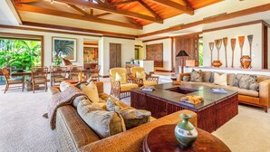 A spacious living area with a high ceiling, wooden beams, a large sofa, a coffee table, and a dining area with chairs and a table.
