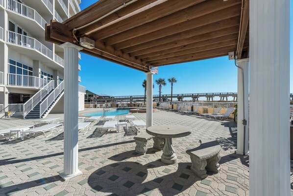 A covered outdoor area with a pool, lounge chairs, and a pergola. - Family Tides - Summerwind 902E (Navarre)
