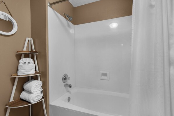 A modern bathroom with a white bathtub, a shower area, and a wooden towel rack with towels.