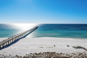 A beach with a long pier extending into the ocean, a sandy shore, and a clear sky.