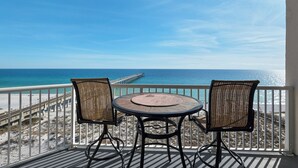 Een balkon met een ronde tafel en twee stoelen, met uitzicht op een strand en een pier.