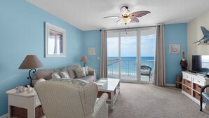 A room with a view of the ocean, a ceiling fan, a sofa, a coffee table, a TV, and a wicker chair. - Hooked On a Feeling - Summerwind 604E (Navarre)