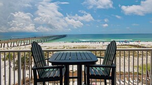 Un balcon avec deux chaises et une table donnant sur une plage avec une jetée.