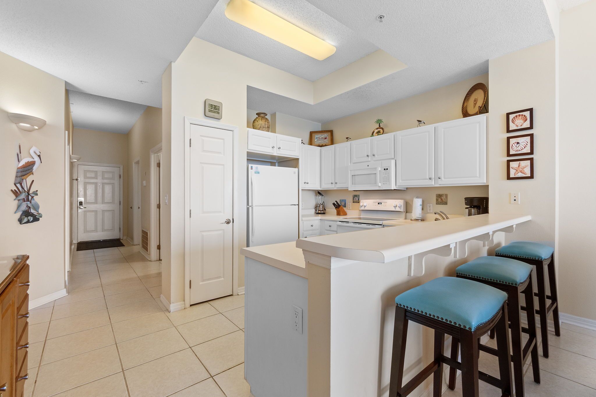 A kitchen with white cabinets, a central island with stools, a refrigerator, and a microwave.