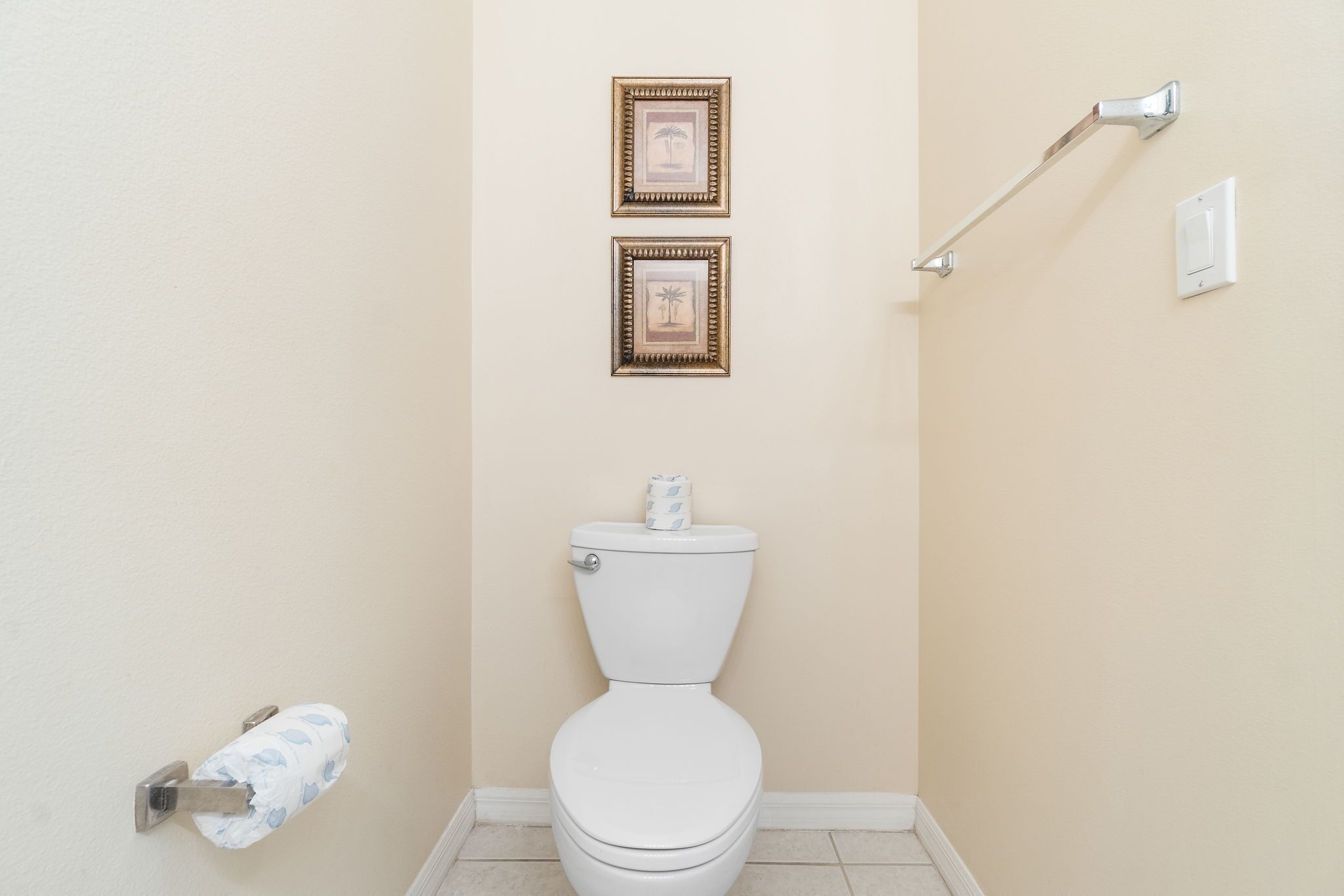 Une salle de bain avec des toilettes, deux tableaux encadrés au mur, un porte-rouleau de papier toilette et une barre d’appui.