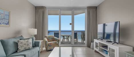 A modern hotel room with a balcony, a flat-screen TV, a sofa, a coffee table, and a chair.