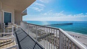 Ein Balkon mit weißen Stühlen und Blick auf Strand und Steg.