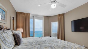 Ein Hotelzimmer mit einem großen Bett, einem Deckenventilator, einem Fernseher und einem Balkon mit Meerblick.