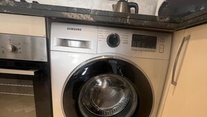 Una lavadora Samsung de carga frontal en una cocina con horno empotrado y un microondas arriba.