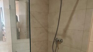 Un baño moderno con mampara de vidrio, ducha, inodoro y lavamanos.