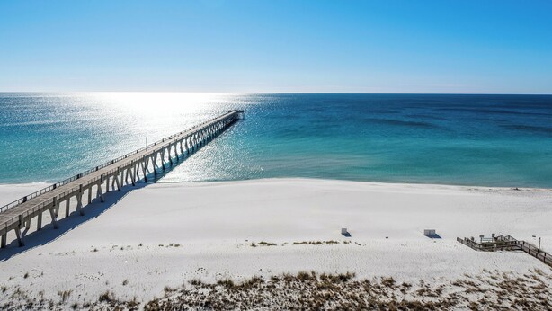 A beach with a long pier extending into the ocean, a sandy shore, and a clear sky. - Oh Whale- Summerwind 1103C (Navarre)