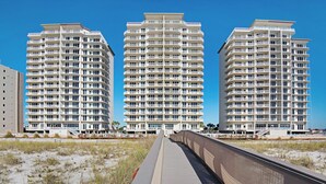 A beachfront hotel with three high-rise buildings, a boardwalk leading to the beach, and a clear blue sky. - Oh Whale- Summerwind 1103C (Navarre)
