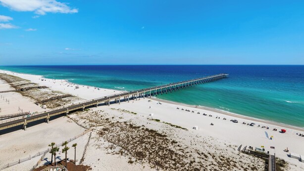 A beach with a long pier extending into the ocean, sandy areas, and a clear blue sky. - Knot a Care- Summerwind 1102C (Navarre)
