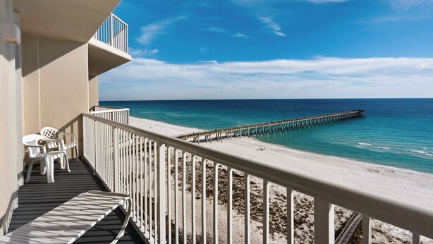 Un balcone con ringhiere bianche che si affaccia su una spiaggia e un molo che si protende sull'oceano.