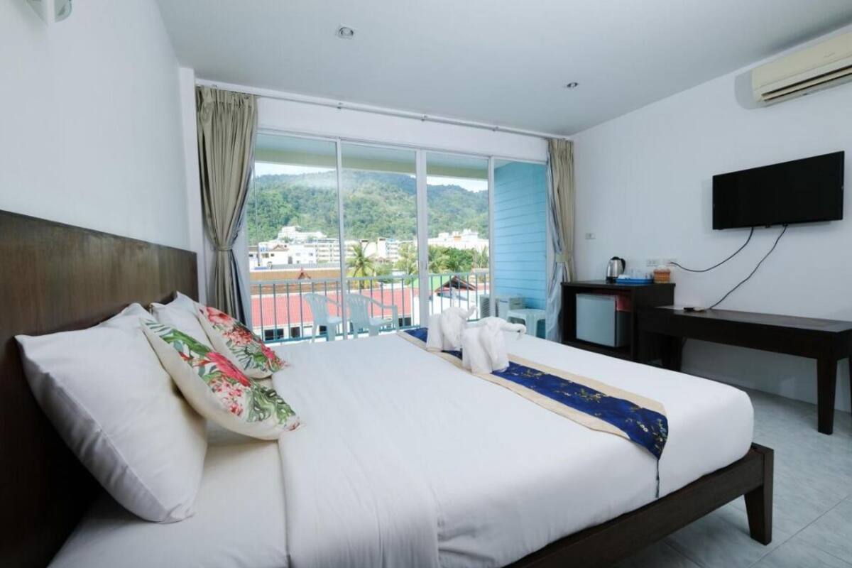 Een hotelkamer met een groot bed, een bureau, een televisie en een balkon met uitzicht op de stad en heuvels.