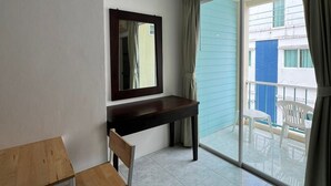 Ein Zimmer mit einem Holztisch, einem Stuhl, einem großen Spiegel und einer Schiebeglastür, die auf einen Balkon mit Sitzmöbeln führt.