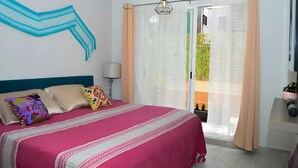 Un dormitorio con cama, almohadas, una mesita de noche, una lámpara y vistas al exterior a través de una puerta de cristal.