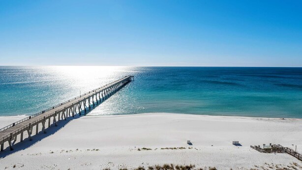Ein Strand mit einer langen Seebrücke, die sich ins Meer erstreckt, wolkenlosem Himmel und ruhiger See.