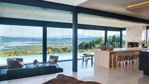 Ein modernes Wohnzimmer mit einem großen Panoramafenster, einem Ledersofa und Blick auf einen Fluss und Berge.