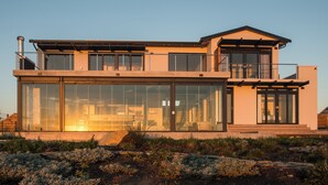 Ein modernes, zweistöckiges Haus mit großen Glasfenstern, einem Flachdach und einem Kiesweg, der zum Eingang führt.