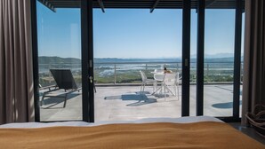 Ein Hotelzimmer mit einem großen Bett, einem Balkon mit Tisch und Stühlen und Blick auf eine Landschaft.
