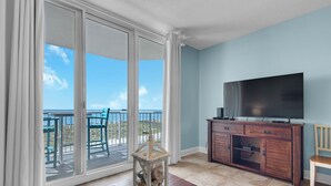 A room with a large sliding glass door leading to a balcony with a view of the beach and ocean.