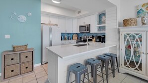 Una cocina moderna con armarios blancos, una isla central con taburetes de bar, un microondas y un horno empotrado.