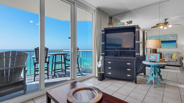 A balcony with a view of the ocean, a TV, and a seating area with a table and chairs.