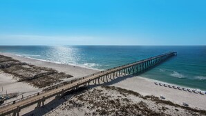 A pier extending into the ocean with a beach on one side and a grassy area on the other.