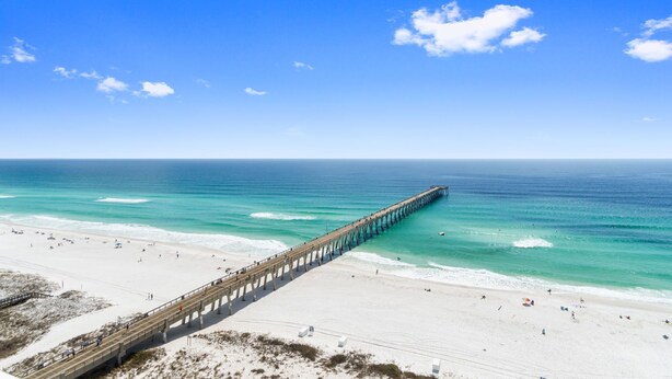 A pier extending into a beach with clear skies and calm waters.