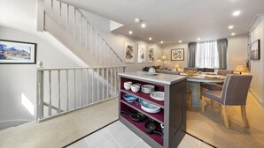 A modern kitchen with a built-in island, a dining area with a table and chairs, and a staircase with a railing. - Modern 3-floor open plan townhouse with patio (London)