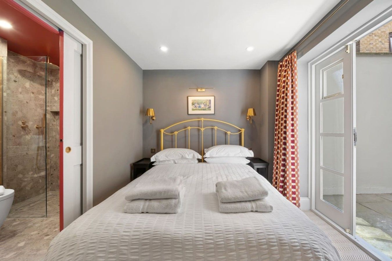 A hotel room with a bed, two bedside tables, a shower, and a door leading to a balcony.