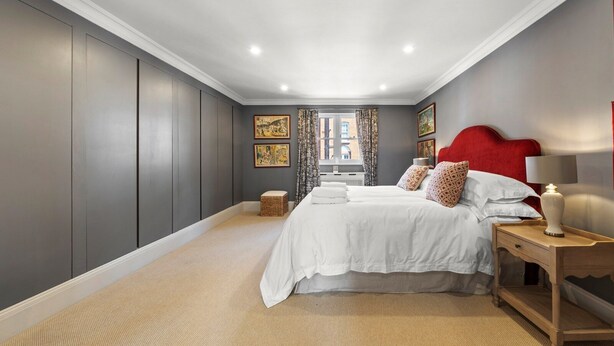 A bedroom with a large bed, a red headboard, a bedside table with a lamp, and a window with curtains. - Modern 3-floor open plan townhouse with patio (London)