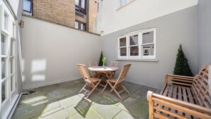 A small patio with a round table and four chairs, a wooden bench, and a small Christmas tree. - Modern 3-floor open plan townhouse with patio (London)