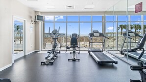 Une salle de sport équipée de machines de cardio, d’un téléviseur et de grandes fenêtres donnant sur une plage.