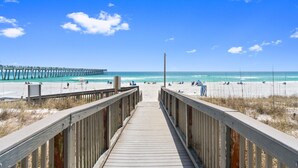 Une promenade en bois qui mène à une plage, avec une jetée en arrière-plan.