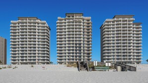 Three high-rise buildings with balconies, a sandy beach in the foreground, and a clear blue sky. - Stow Away - Summerwind 101C (Navarre)