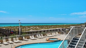 A pool area with lounge chairs and a hot tub, overlooking a beach with clear blue water. - Stow Away - Summerwind 101C (Navarre)
