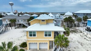 A beachfront property with a two-story house featuring a garage, a covered patio, and a view of the ocean. - PIECE OF SUNSHINE! 20% LOWER RATES NOW THROUGH THE END OF THE YEAR! (Navarre)