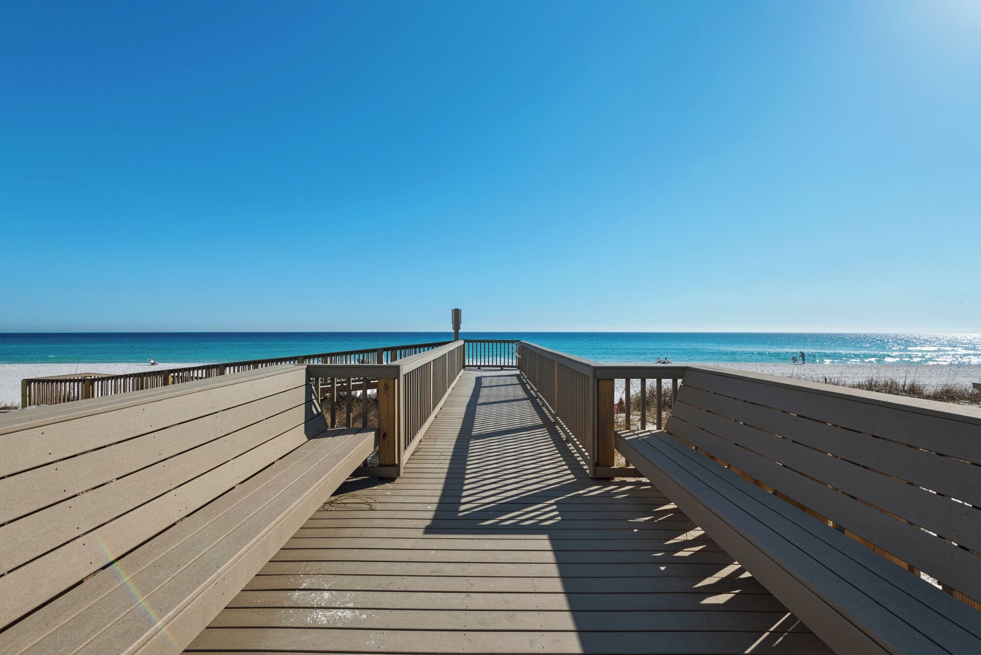 Eine Holzpromenade führt zu einem Strand unter blauem Himmel.