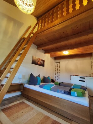 A cozy bedroom with a wooden staircase, a bed with colorful pillows, a bedside table, and a wall-mounted lamp. - Quietly located vacation apartment in the countryside - with terrace and garden (Rotthalmünster)