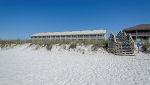 A beachfront hotel with a long building, a staircase leading to a covered area, and a sandy beach.