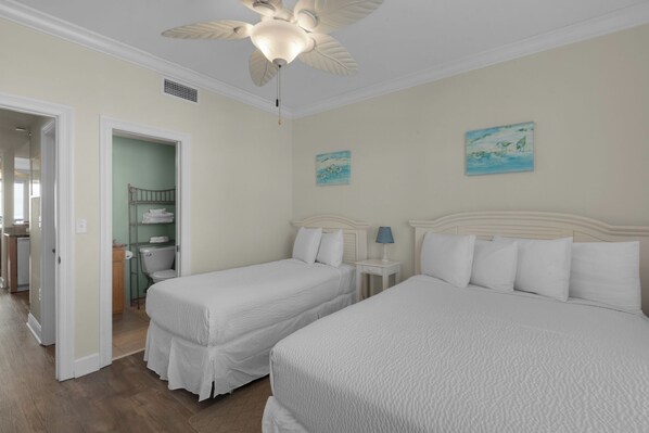 Une chambre avec deux lits, un ventilateur de plafond et des œuvres d’art accrochées aux murs.