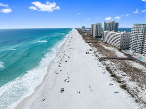 A beach with a long stretch of sand, a few umbrellas, and tall buildings in the background.
