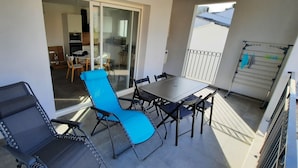 A balcony with a dining table and chairs, a blue lounge chair, and a metal drying rack.