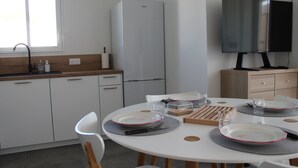 A modern kitchen with white cabinets, a built-in refrigerator, a dining table set with plates, glasses, and cutlery.